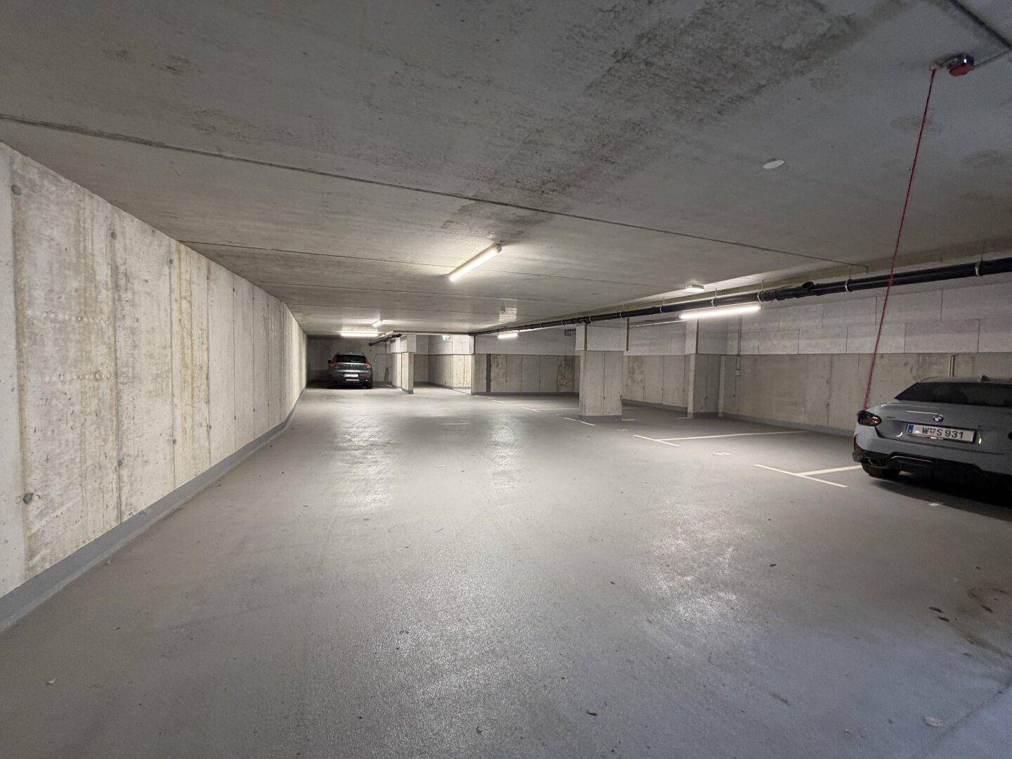 Weitläufige Tiefgarage mit Betonstruktur und markierten Stellplätzen für Bewohner.