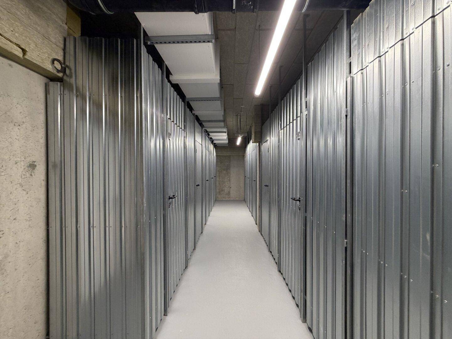 Gang in der Tiefgarage mit zahlreichen abschließbaren Abstellräumen aus Metall.