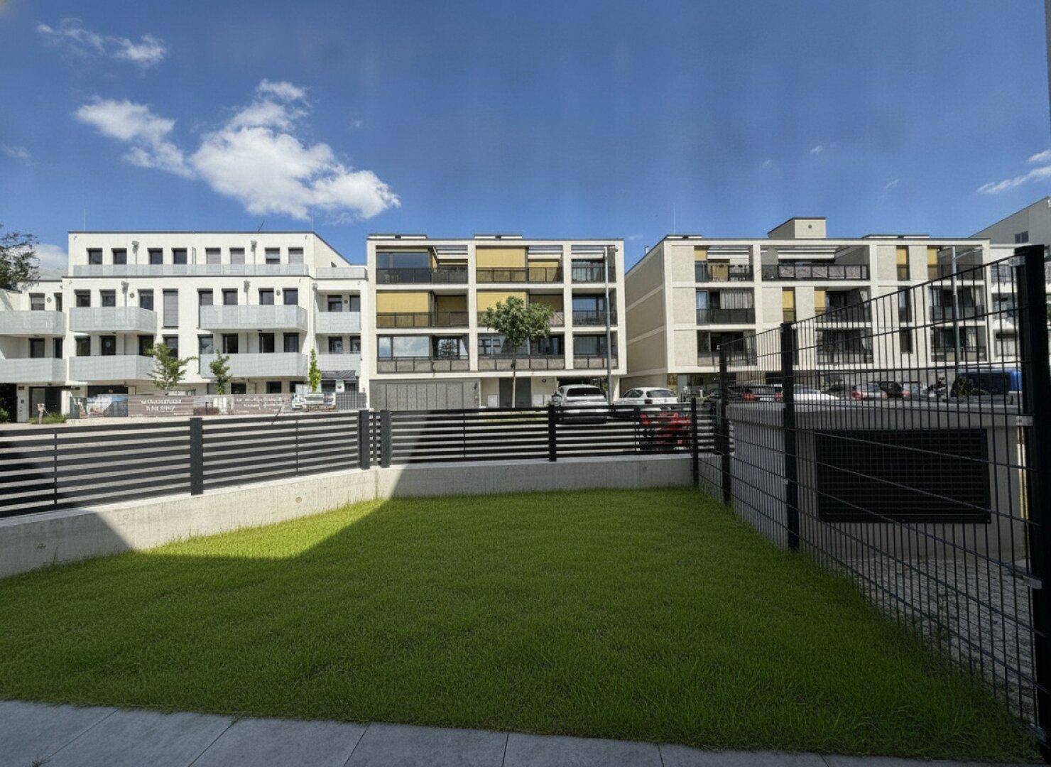Blick auf moderne Wohngebäude mit Balkonen und einem grünen Rasenbereich im Vordergrund.