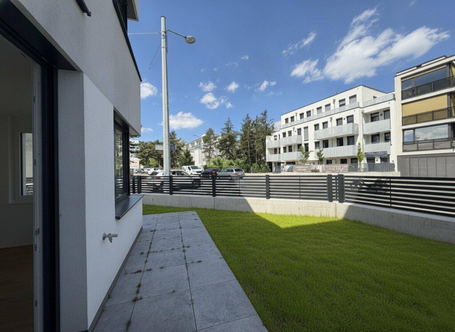 Seitenansicht des Gebäudes mit gepflastertem Weg, Rasenfläche und Blick auf die Umgebung.