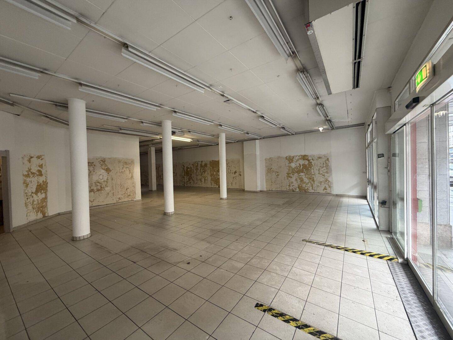 Weitläufiger Ladenraum mit Fliesenboden, Säulen und großen Fenstern, bereit für die Neugestaltung.