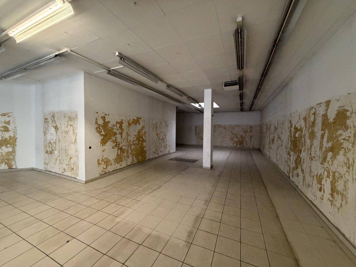 Hinterer Bereich des Geschäftsraums mit Fliesenboden, einer Säule und abgenutzten Wänden, bereit zur Renovierung.