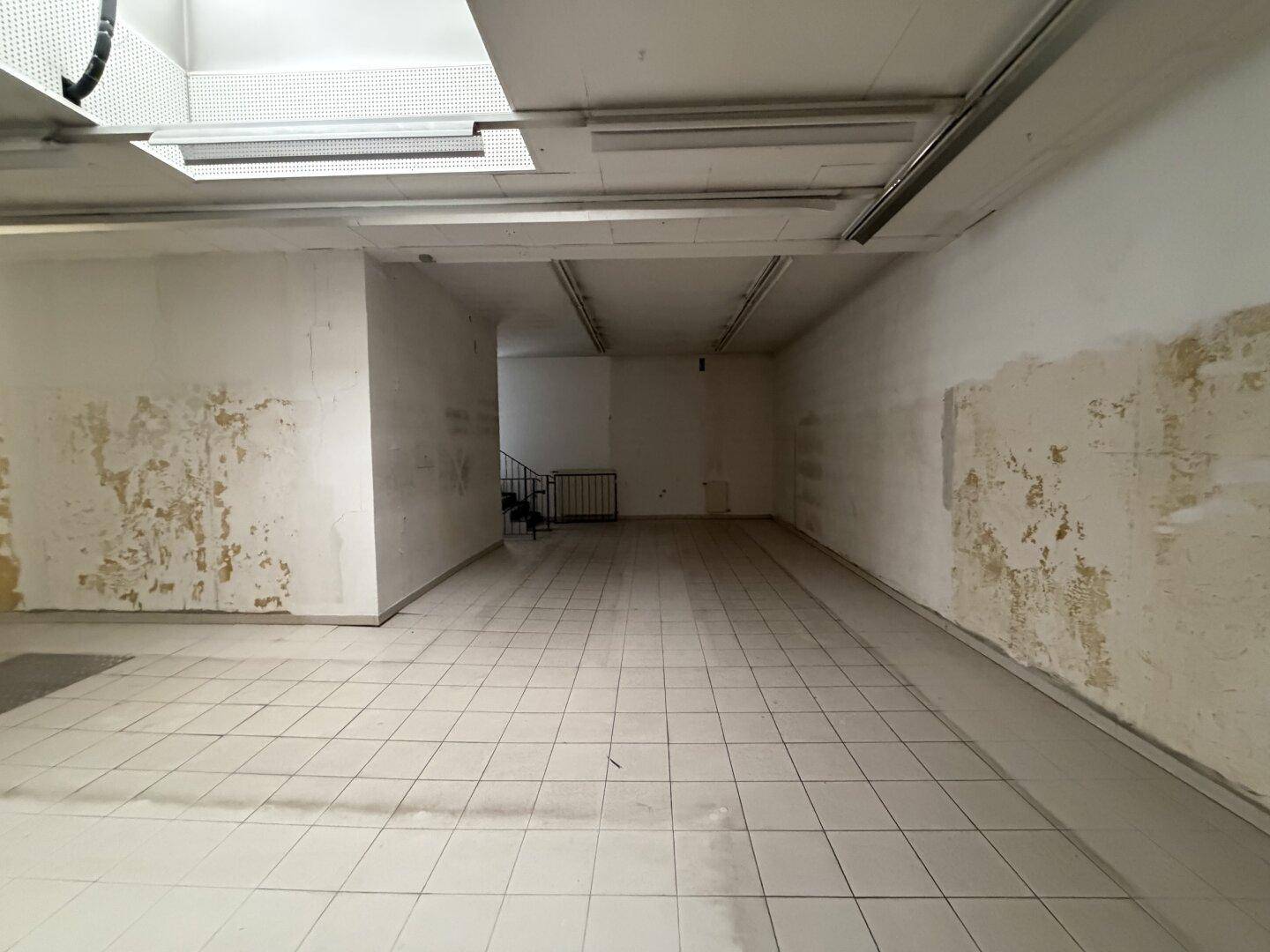 Hinterer Bereich des Geschäftsraums mit Fliesenboden und einer Treppe im Hintergrund, die zu weiteren Ebenen führt.