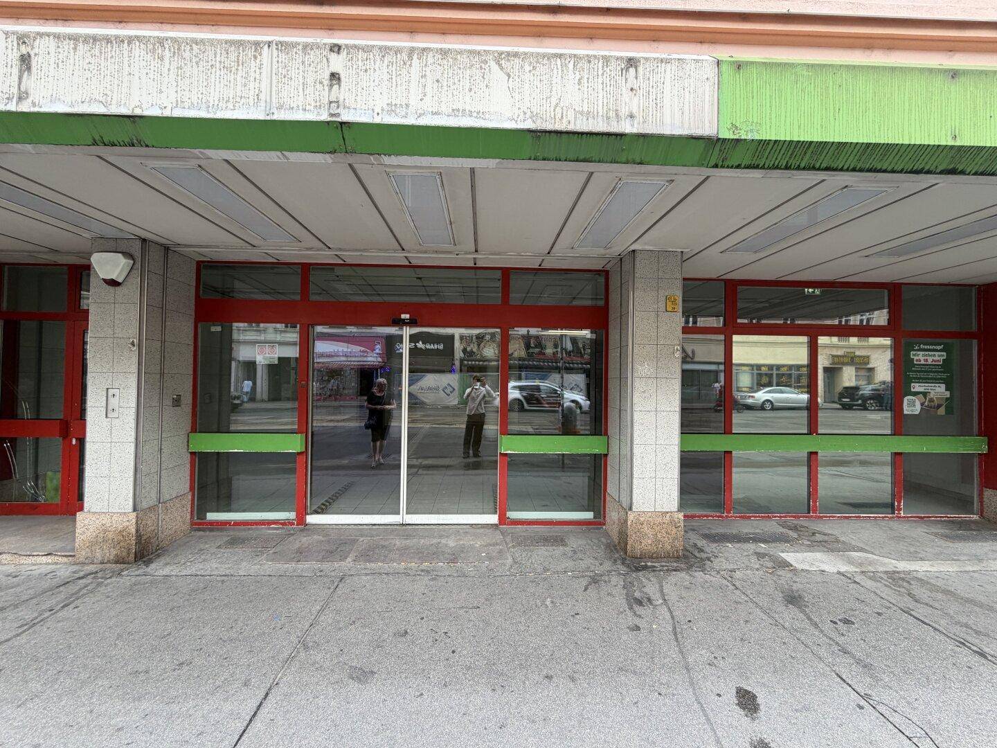 Eingangsbereich des Gebäudes mit roten Türrahmen, großen Glasflächen und grünen Akzenten an der Fassade.
