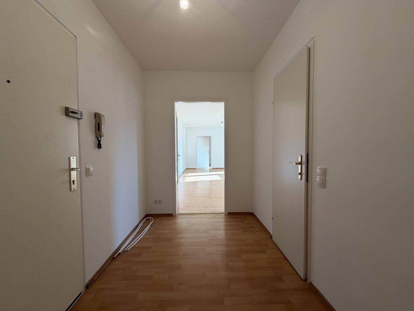 Heller Flur mit Laminatboden und weißen Wänden, der zu weiteren Räumen führt.