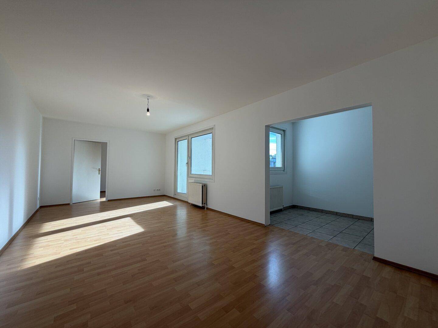Geräumiger Wohnbereich mit Laminatboden und offenem Durchgang zu einem gefliesten Bereich.