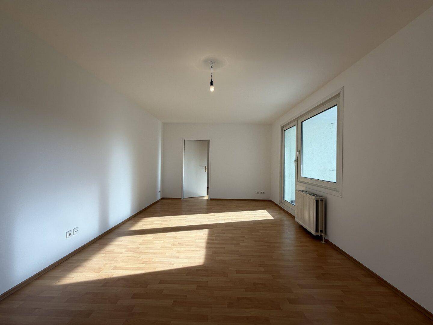 Helles Zimmer mit Laminatboden und großen Fenstern, das viel Sonnenlicht empfängt.