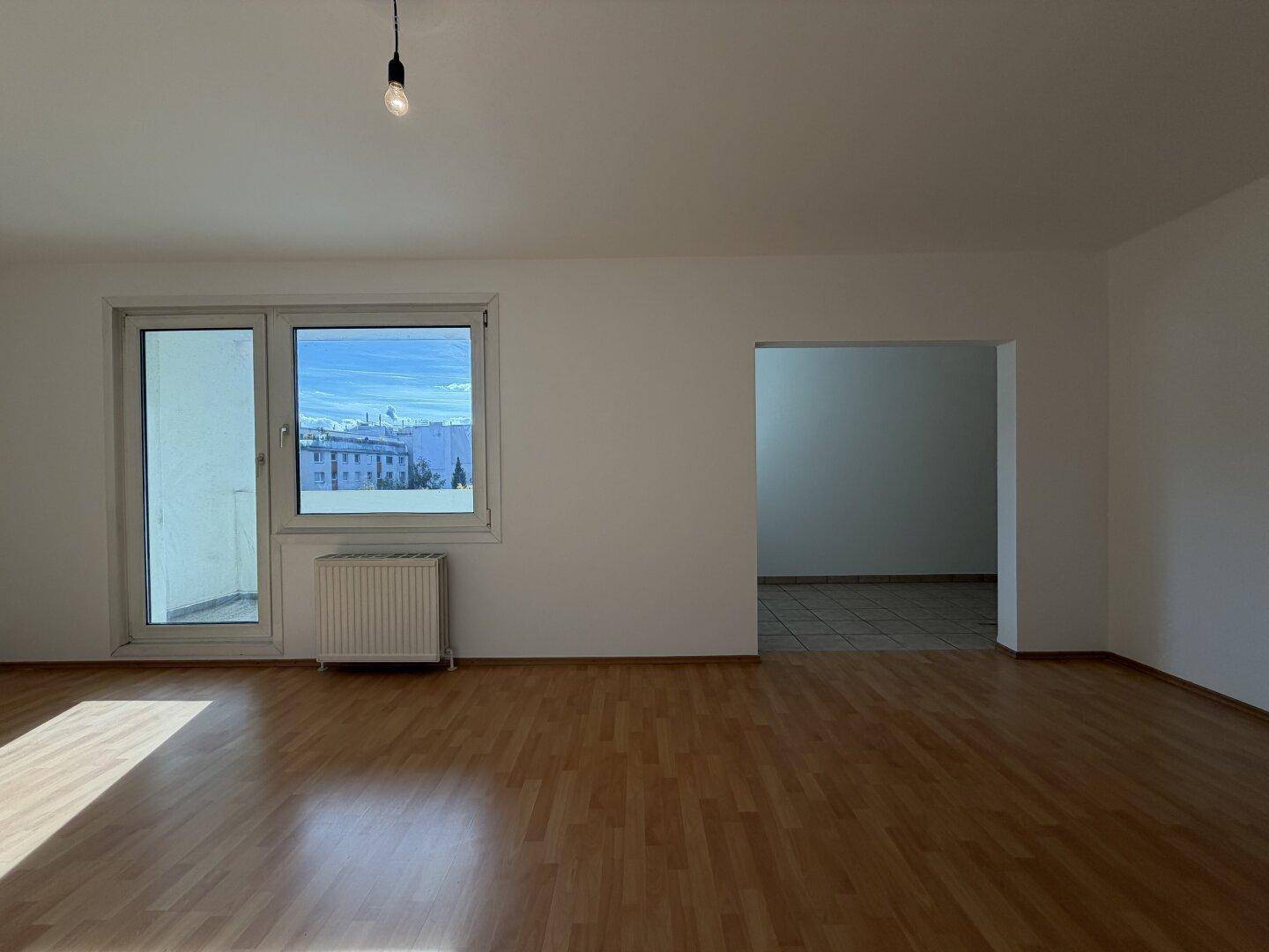 Wohnbereich mit Laminatboden und Zugang zum Balkon, verbunden mit einem gefliesten Raum.