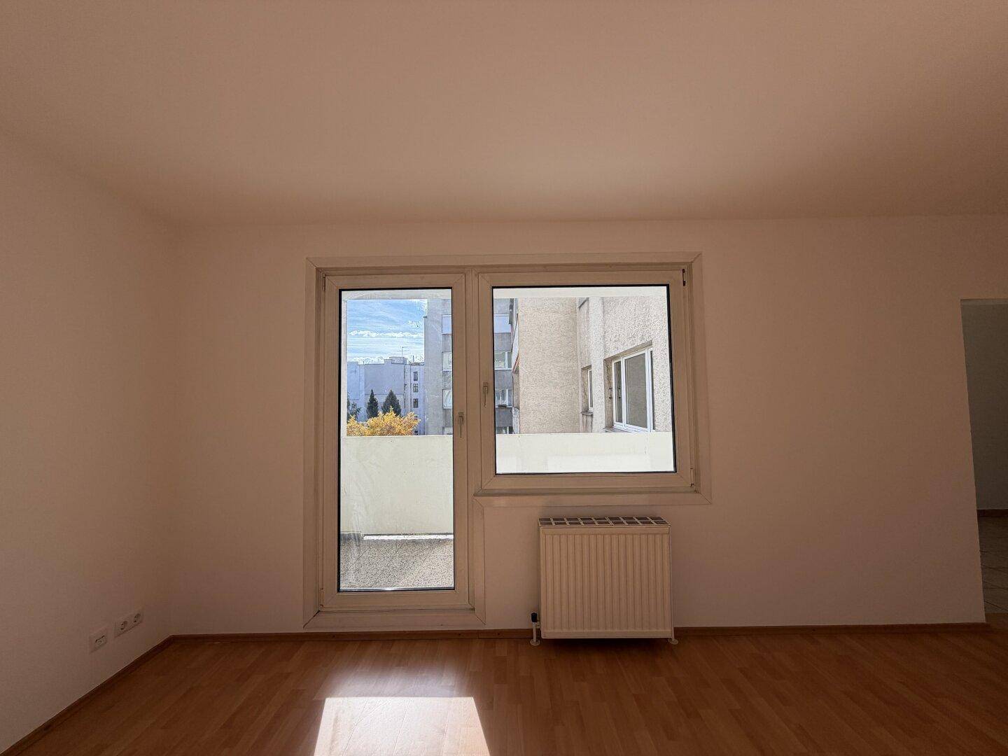 Heller Raum mit Laminatboden und Fensterfront, die Zugang zu einem Außenbereich bietet.