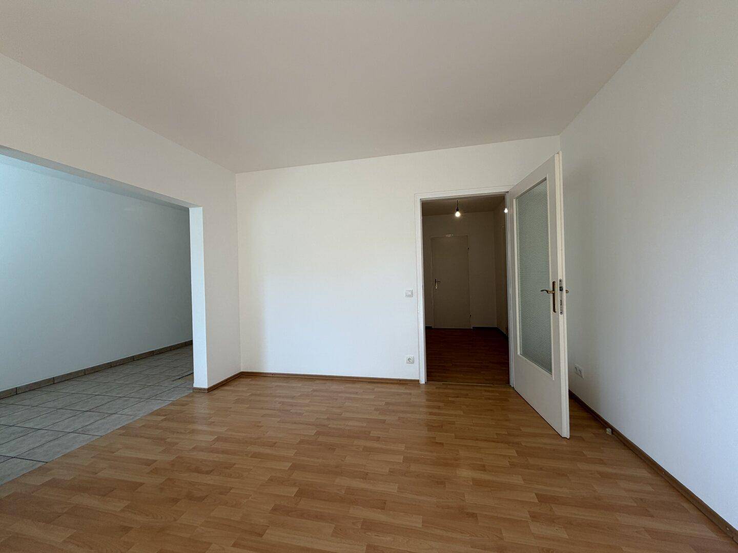 Wohnbereich mit Laminatboden und offenem Durchgang zu einem gefliesten Bereich.