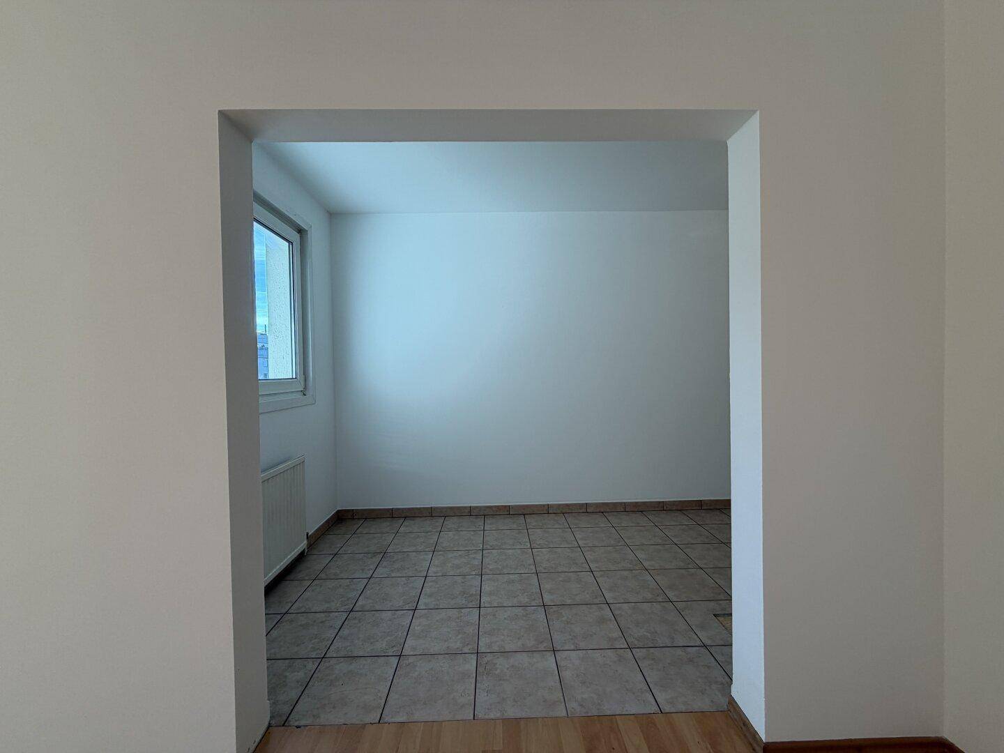 Heller, gefliester Raum mit Fenster und Heizkörper, ideal als Küche oder Essbereich.