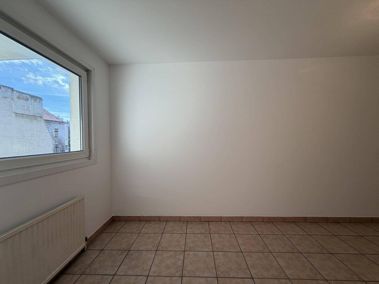 Geräumiger, gefliester Raum mit Fenster, der sich gut als Küche oder Esszimmer eignet.