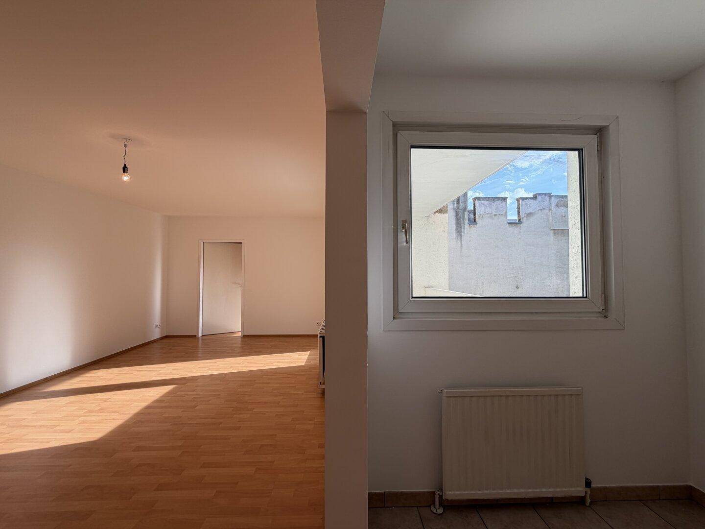 Blick vom gefliesten Bereich in den hellen Wohnraum mit Laminatboden und viel Sonnenlicht.