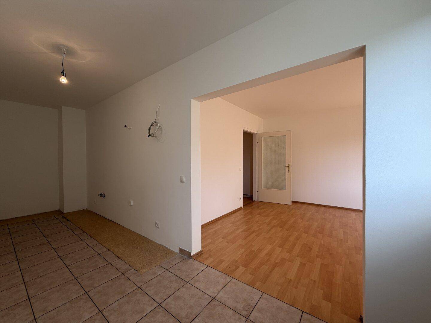 Blick vom gefliesten Küchenbereich in den angrenzenden Wohnraum mit Laminatboden.