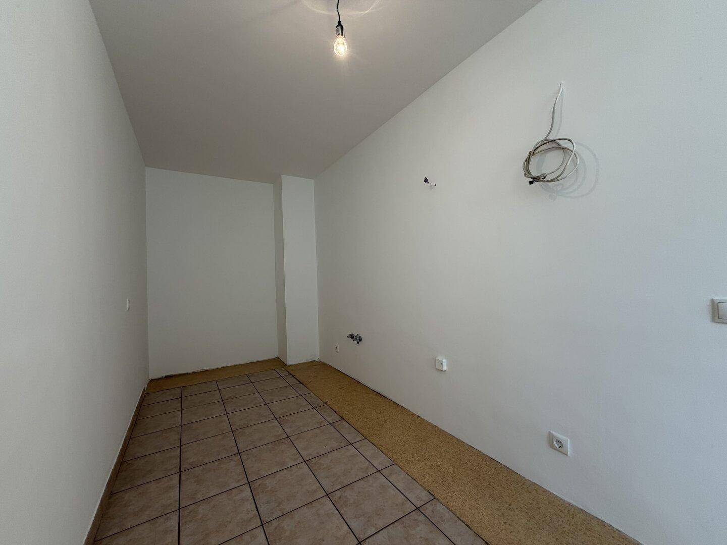 Leerer, gefliester Raum mit weißen Wänden und sichtbaren Elektroinstallationen für die Küche.