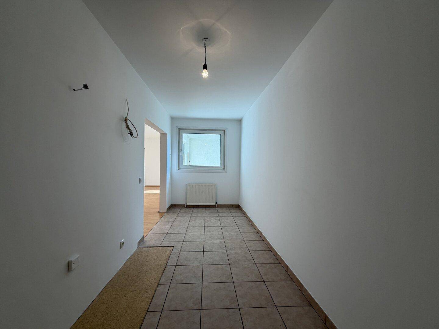 Heller, gefliester Raum mit Fenster und Heizkörper, der sich als Küche oder Hauswirtschaftsraum eignet.