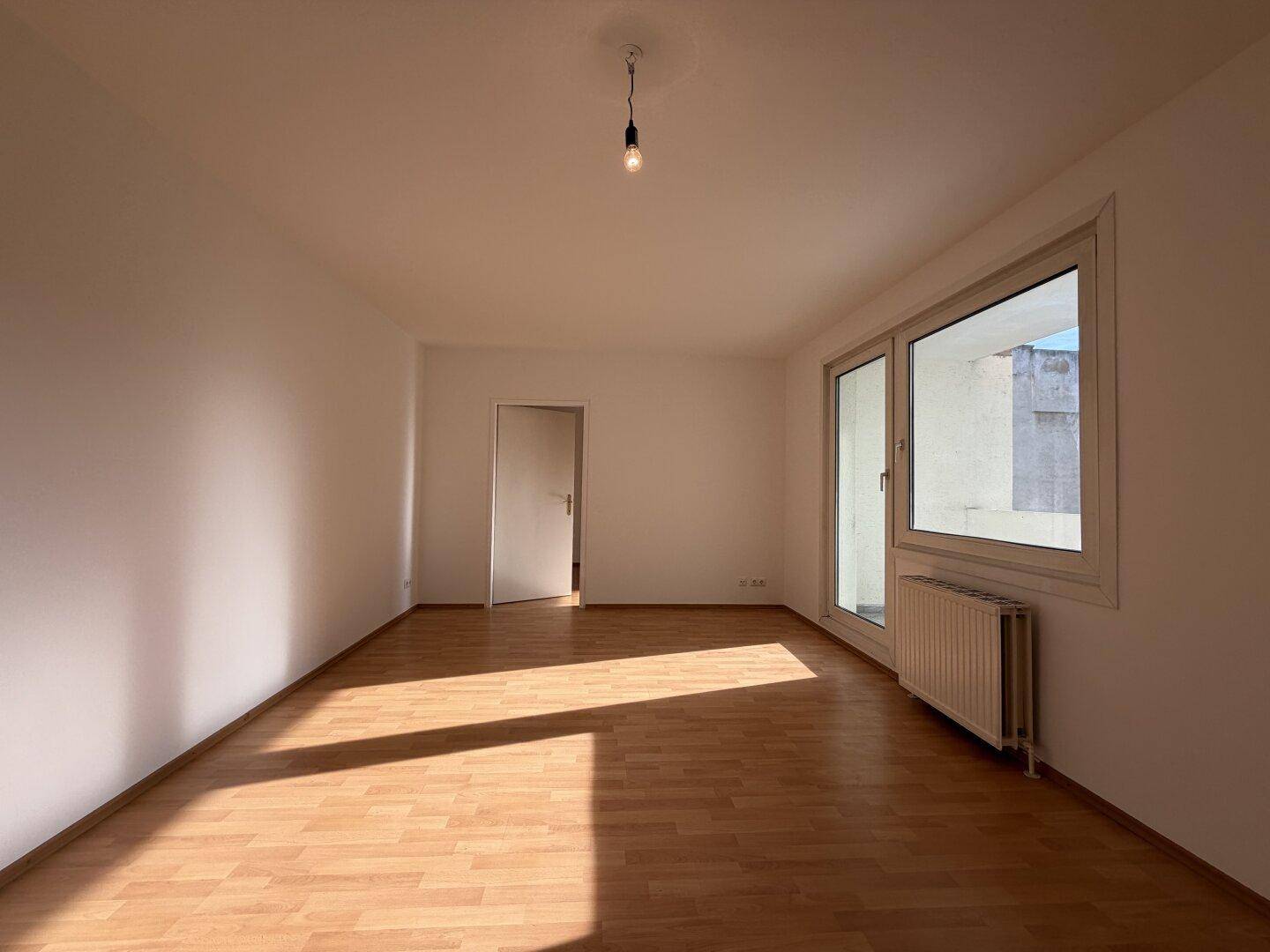 Geräumiges, helles Zimmer mit Laminatboden und großem Fenster, das viel Sonnenlicht einfängt.
