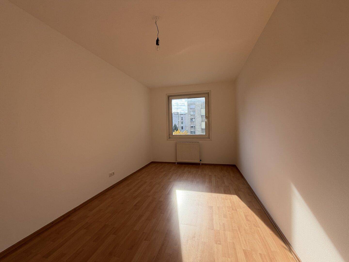 Helles Schlafzimmer mit Laminatboden und Fenster, das eine ruhige Atmosphäre schafft.