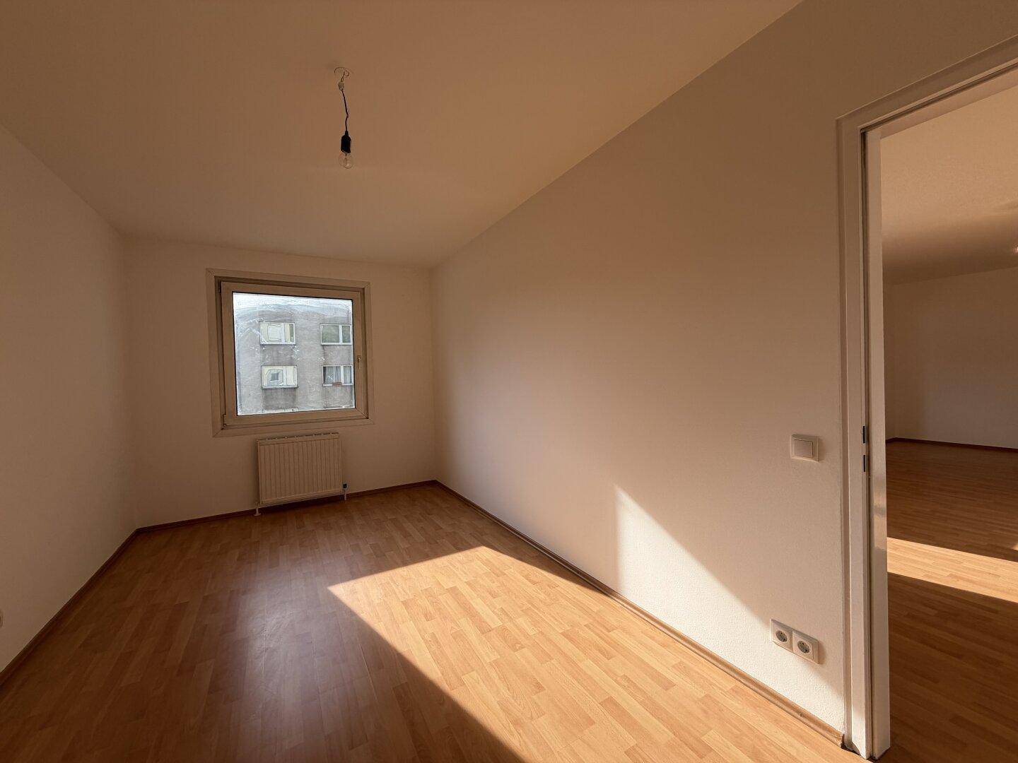 Helles Zimmer mit Laminatboden und Fenster, das viel Tageslicht hereinlässt und einen ruhigen Rückzugsort bietet.