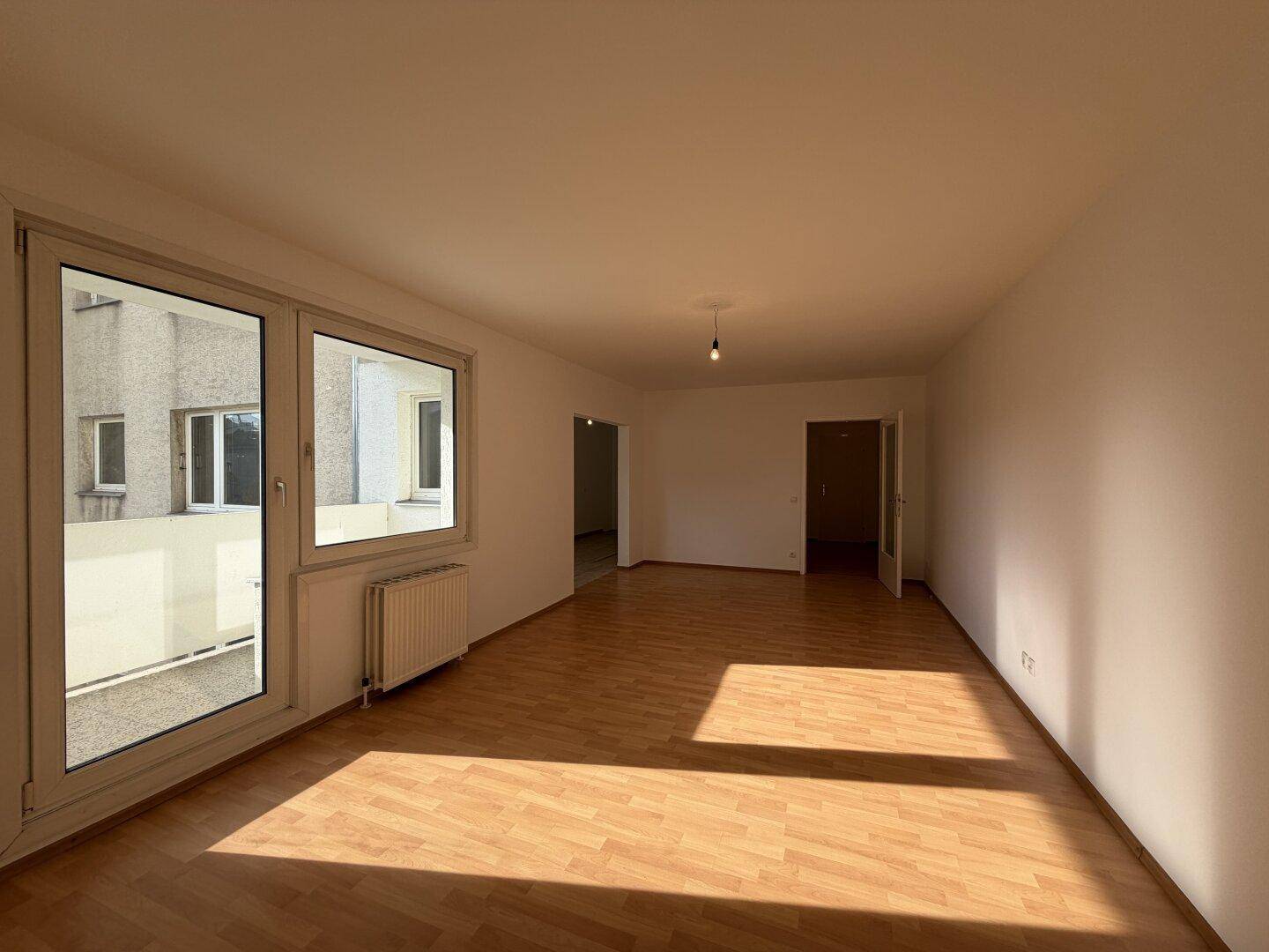 Geräumiges Wohnzimmer mit Laminatboden und Zugang zum Balkon, das viel natürliches Licht erhält.