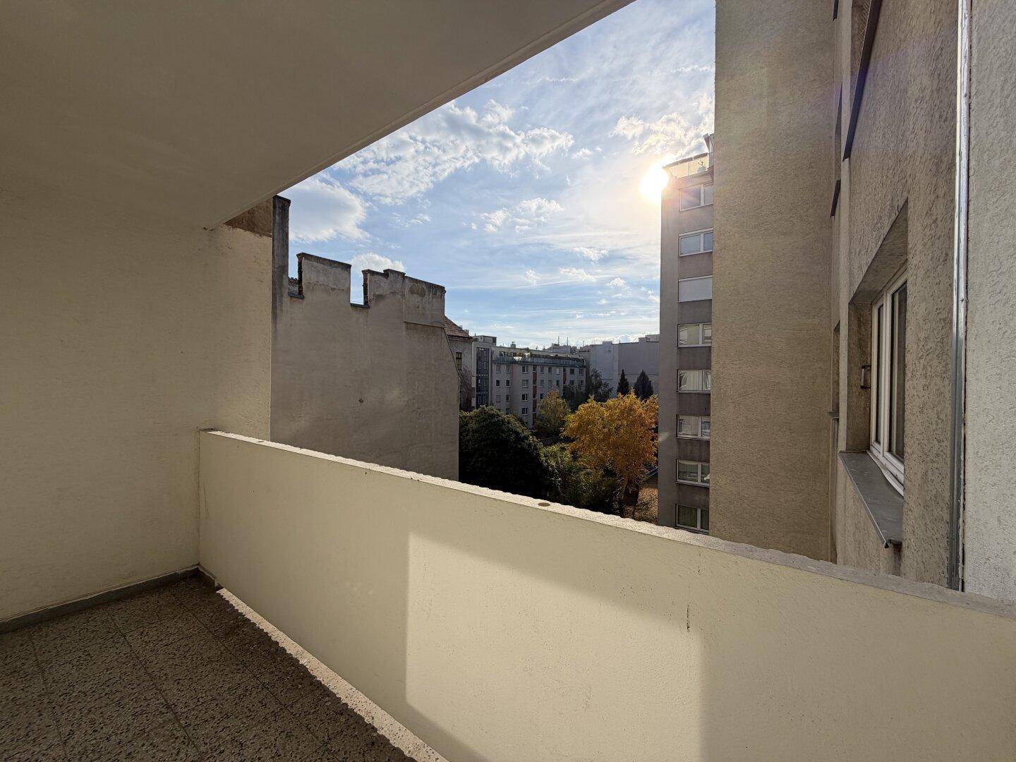 Heller Balkon mit Fliesenboden, der einen weiten Blick über die Stadt und grüne Bäume bietet.