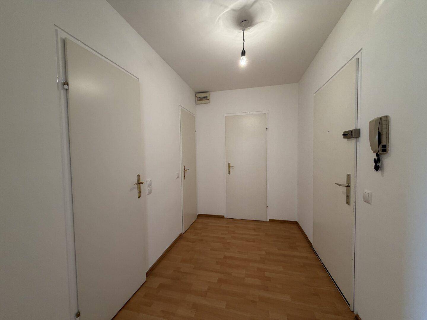 Heller Flur mit Laminatboden und mehreren weißen Türen, der verschiedene Räume verbindet.
