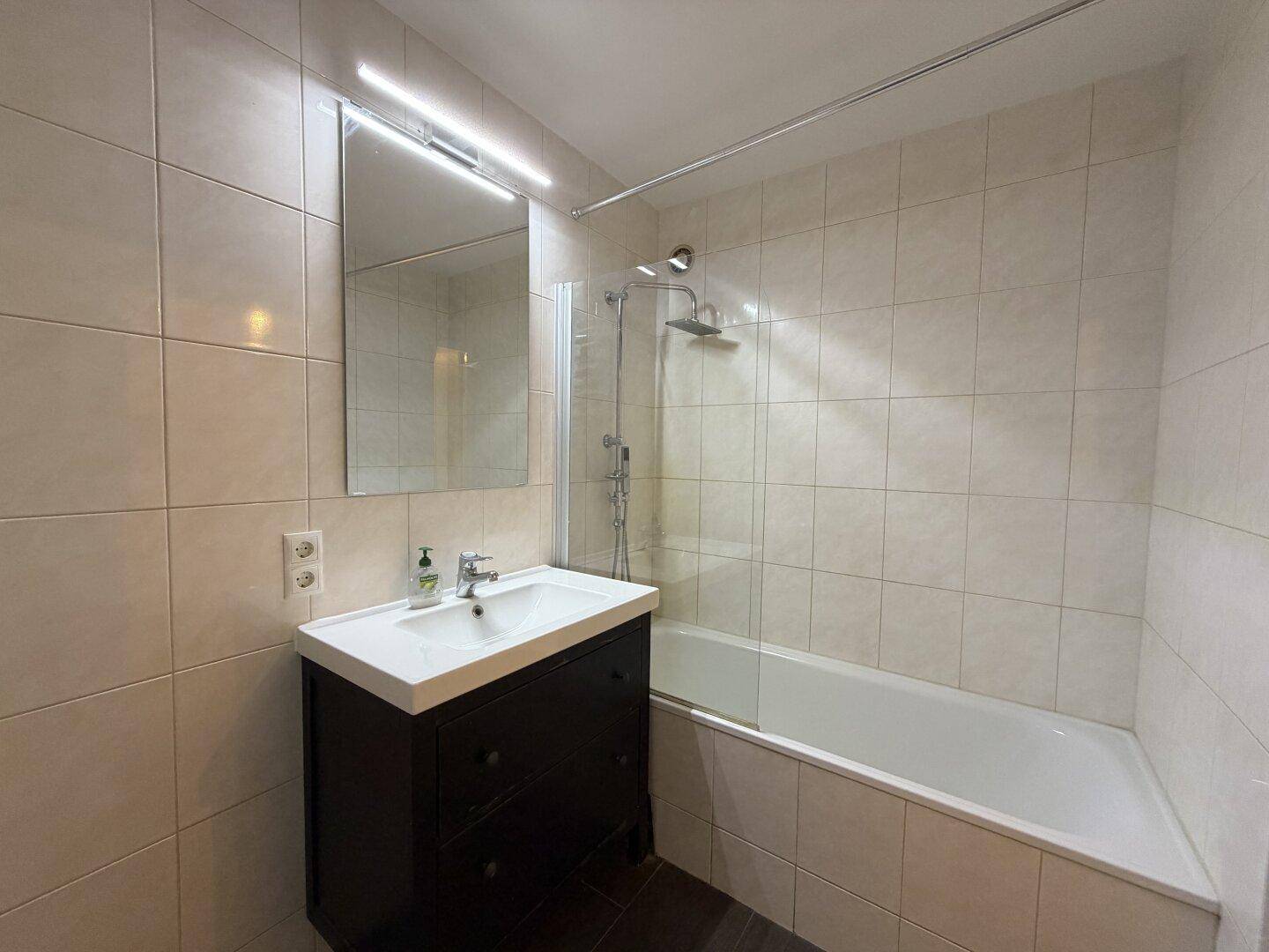 Modernes Badezimmer mit Badewanne, Duschvorrichtung und einem einzelnen Waschbecken mit dunklem Unterschrank.