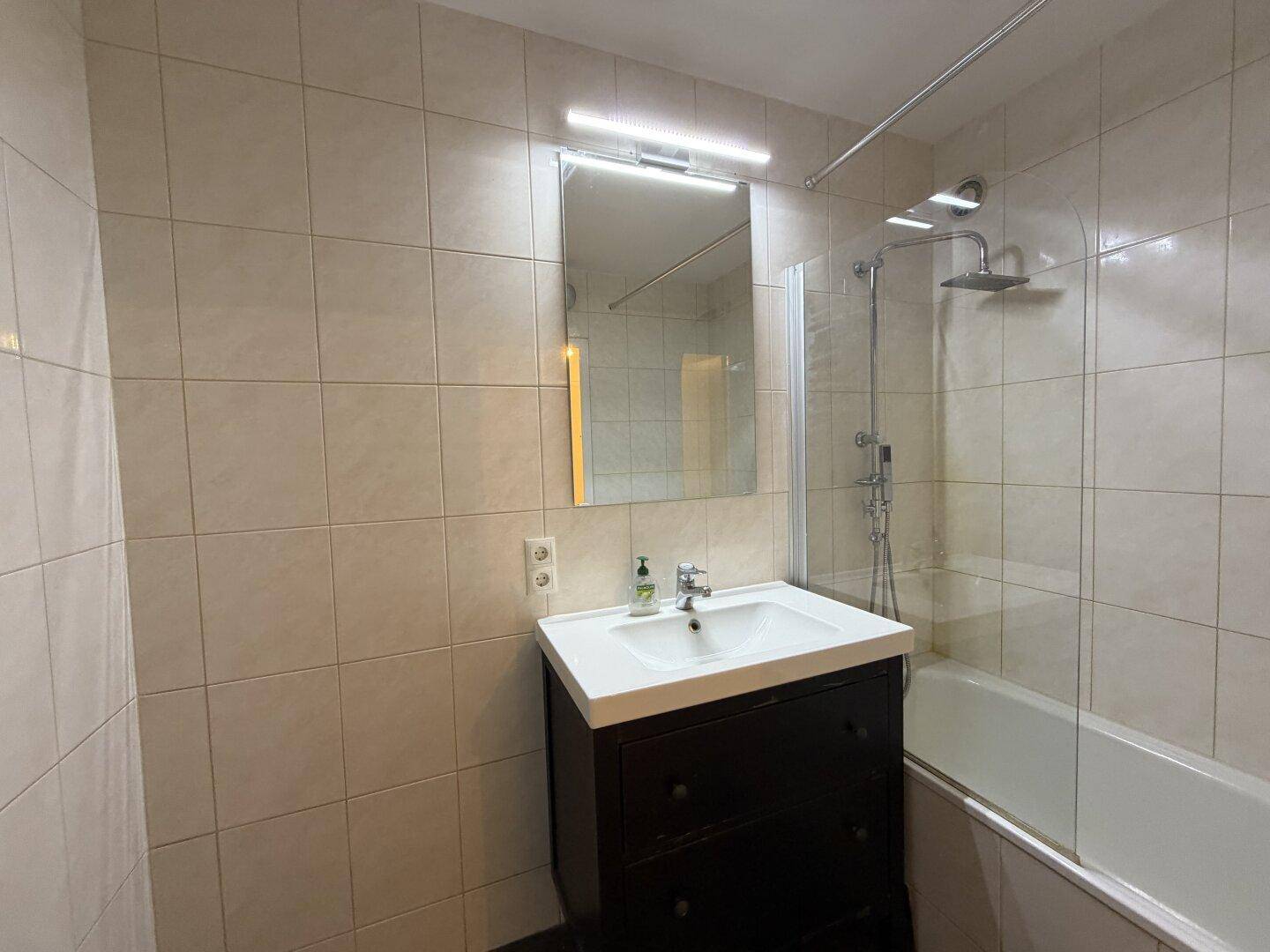 Modernes Badezimmer mit Badewanne, Duschvorrichtung und einem einzelnen Waschbecken mit dunklem Unterschrank.