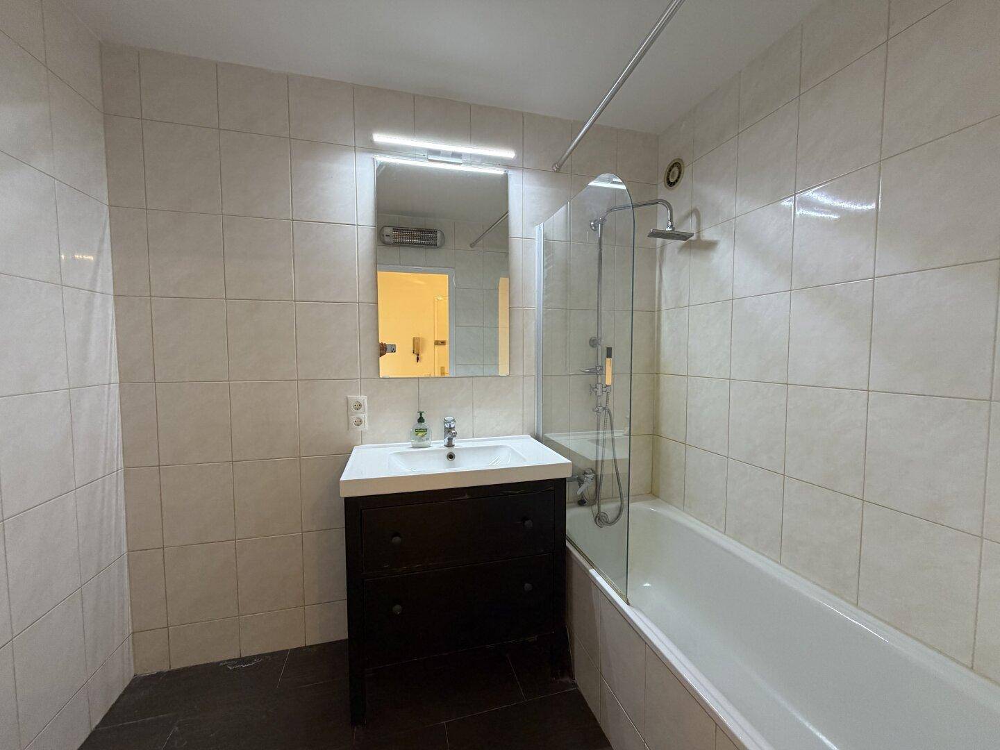 Modernes Badezimmer mit Badewanne, Duschvorrichtung und einem einzelnen Waschbecken mit dunklem Unterschrank.