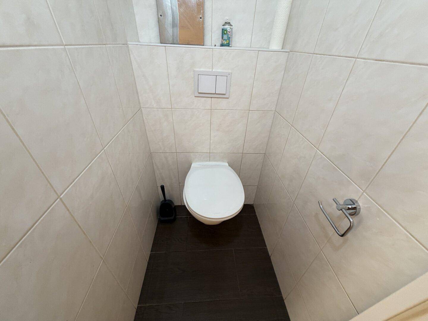 Separate Toilette mit Wand-WC und hellen Fliesen an den Wänden sowie dunklem Boden.