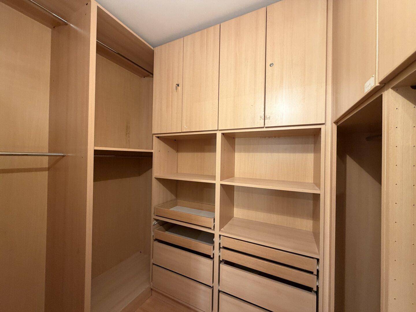 Geräumiger begehbarer Kleiderschrank mit vielen Ablagen, Schubladen und Hängemöglichkeiten aus hellem Holz.