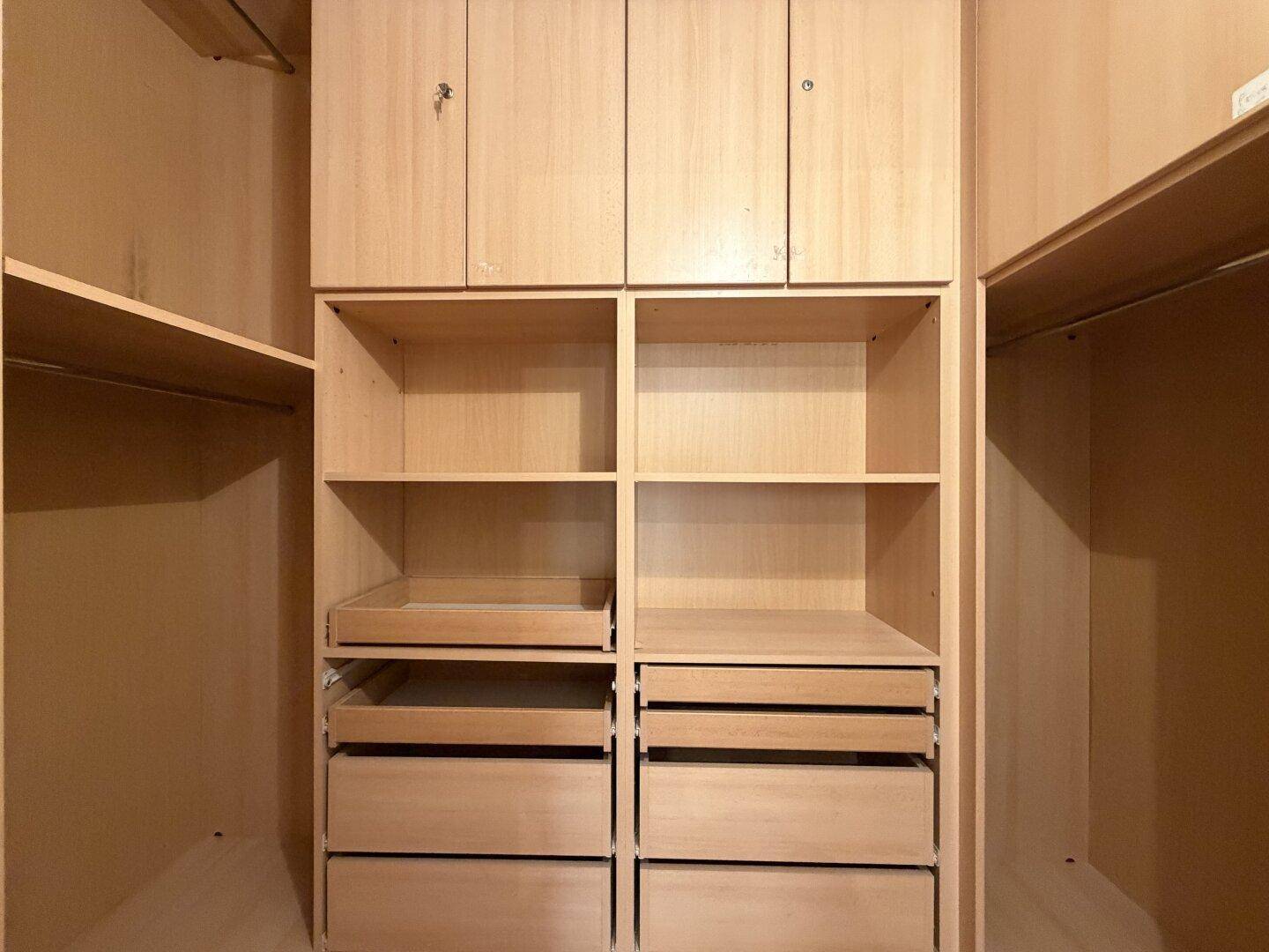 Geräumiger begehbarer Kleiderschrank mit vielen Ablagen, Schubladen und Hängemöglichkeiten aus hellem Holz.