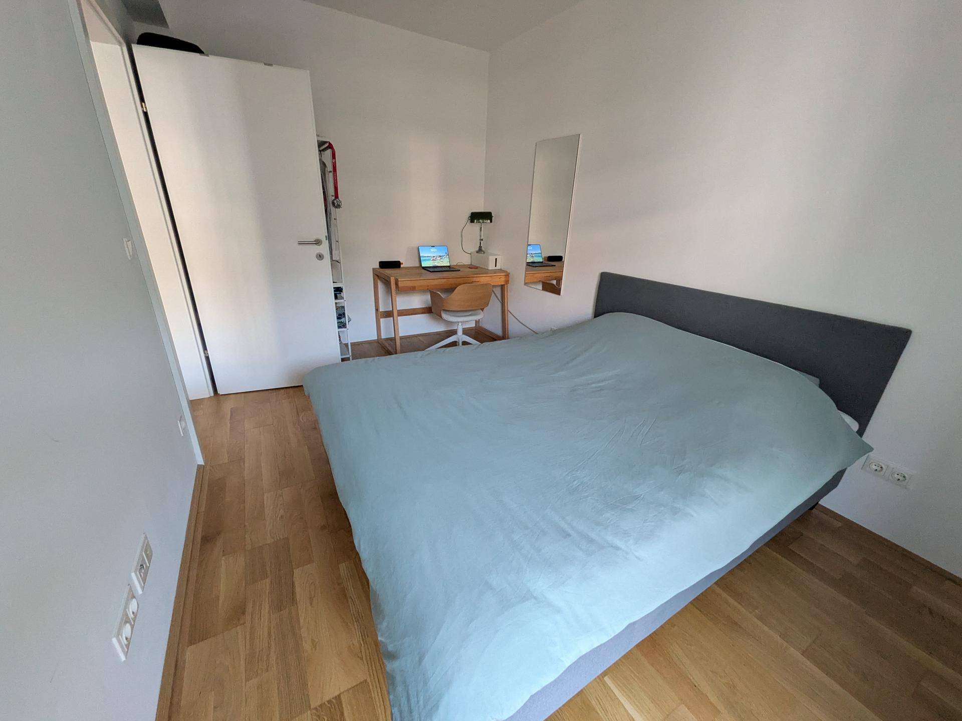 Schlafzimmer mit Holzboden, Bett, Schreibtisch und einem Kleiderschrank.