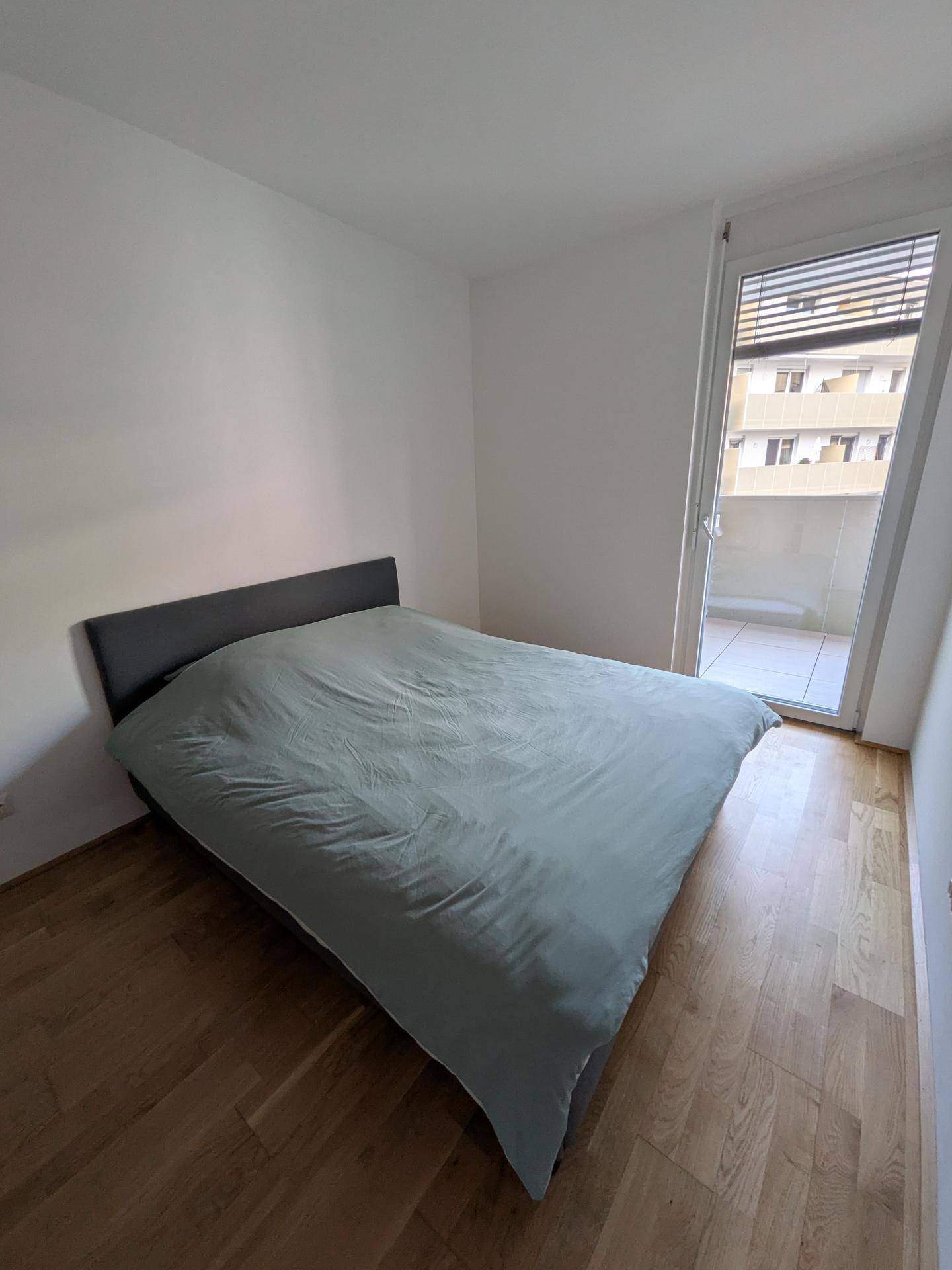 Schlafzimmer mit Holzboden, Doppelbett und direktem Zugang zum Balkon.