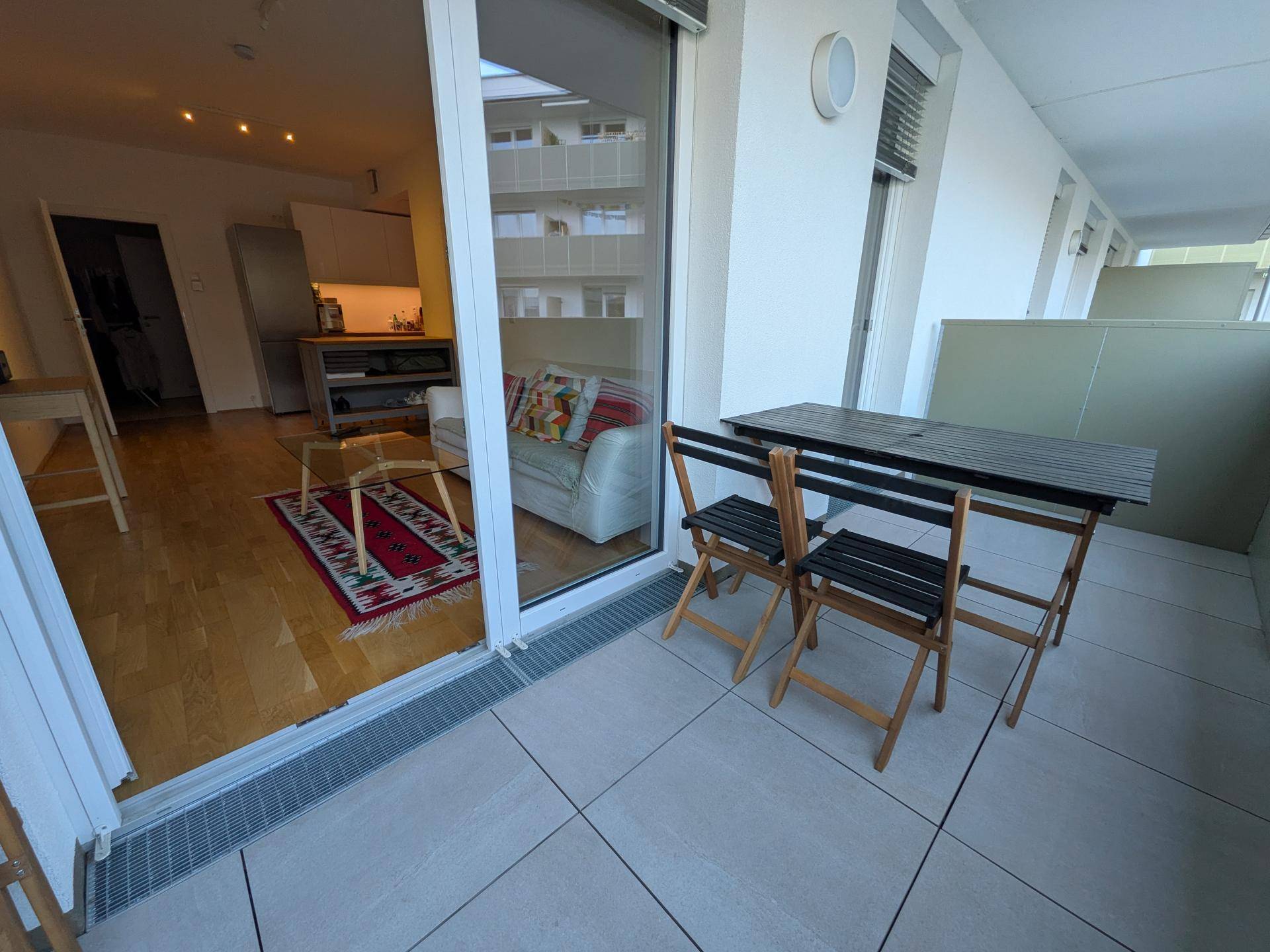 Balkon mit Fliesenboden und Sitzgelegenheiten, mit Blick in den Wohnbereich.