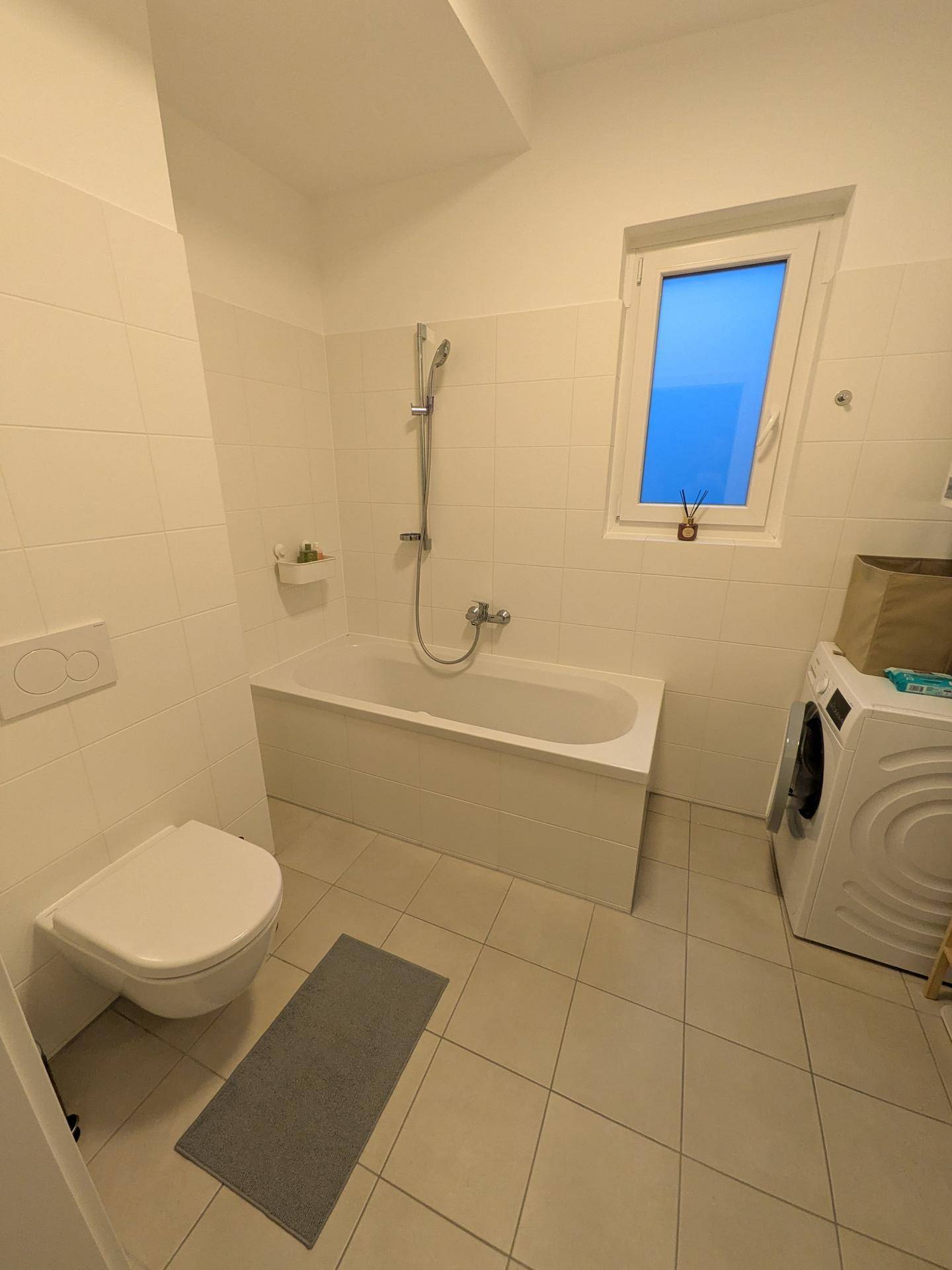 Modernes Badezimmer mit Badewanne, Toilette, Waschmaschine und Fenster.