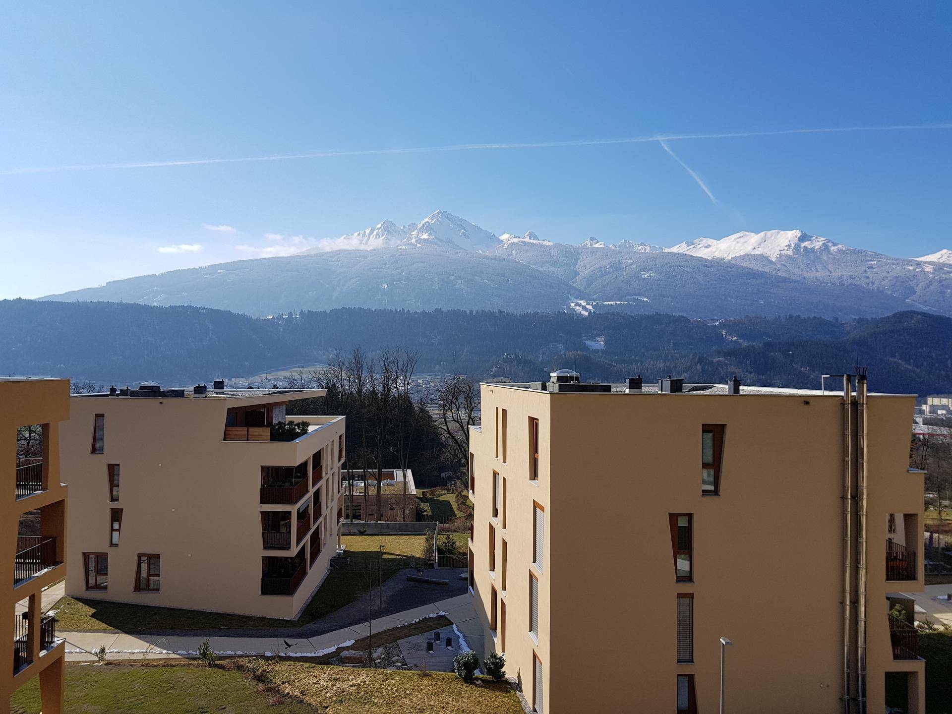 Moderne Wohngebäude in einer grünen Umgebung mit beeindruckendem Panorama der schneebedeckten Berge im Hintergrund.
