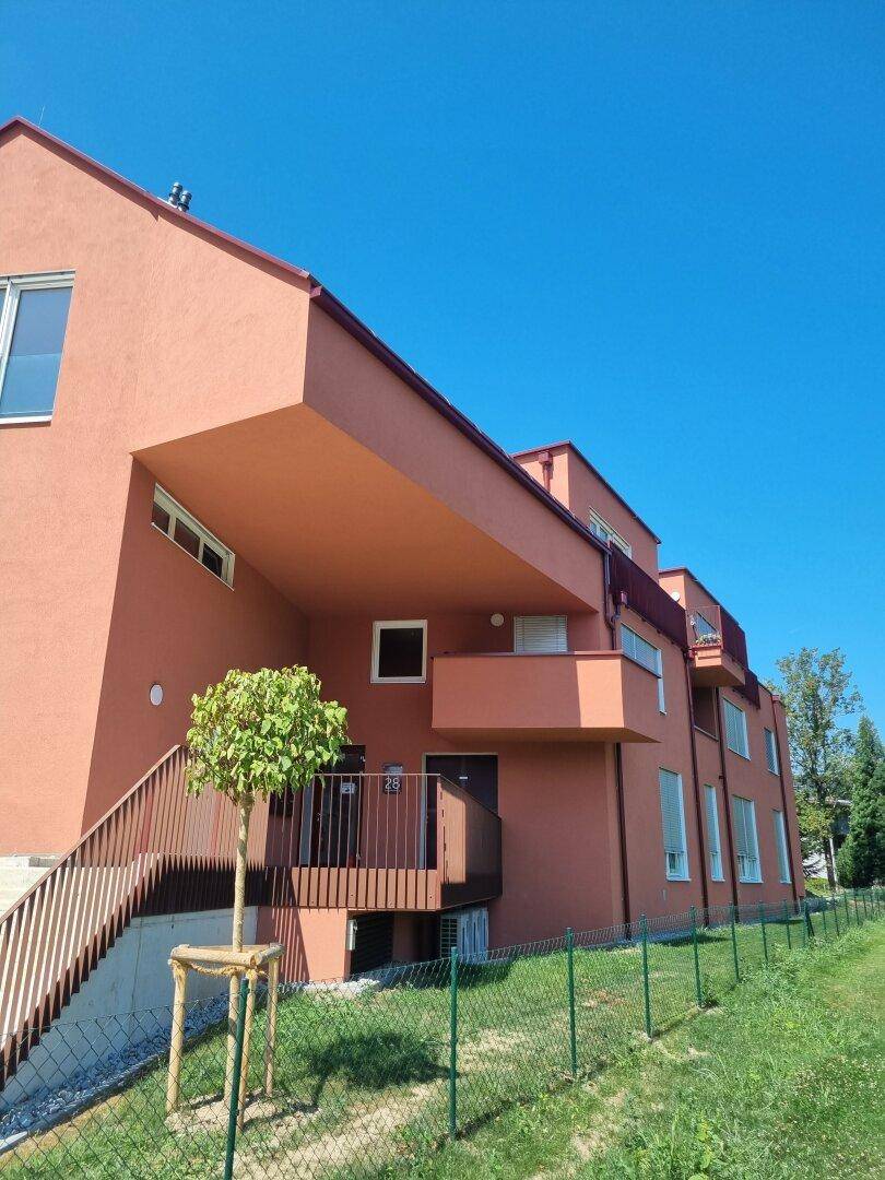 Ansicht des modernen Wohngebäudes mit roter Fassade, Balkonen und Zugangsbereich.
