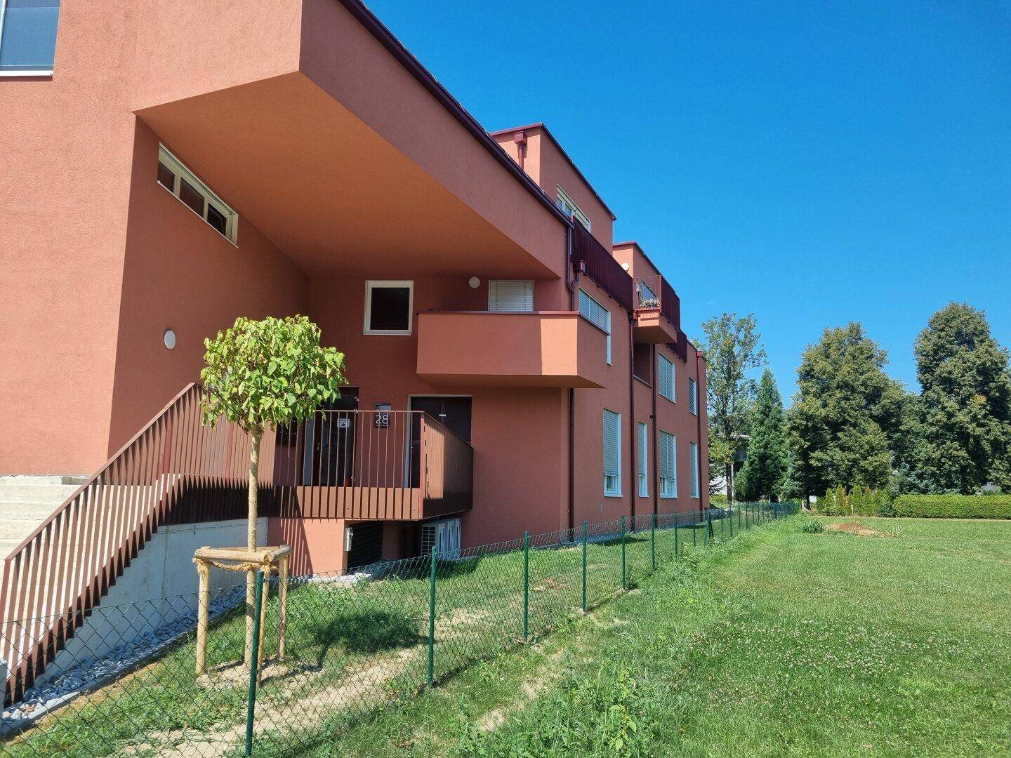 Seitenansicht des Wohngebäudes mit roter Fassade, Balkonen und gepflegter Rasenfläche.