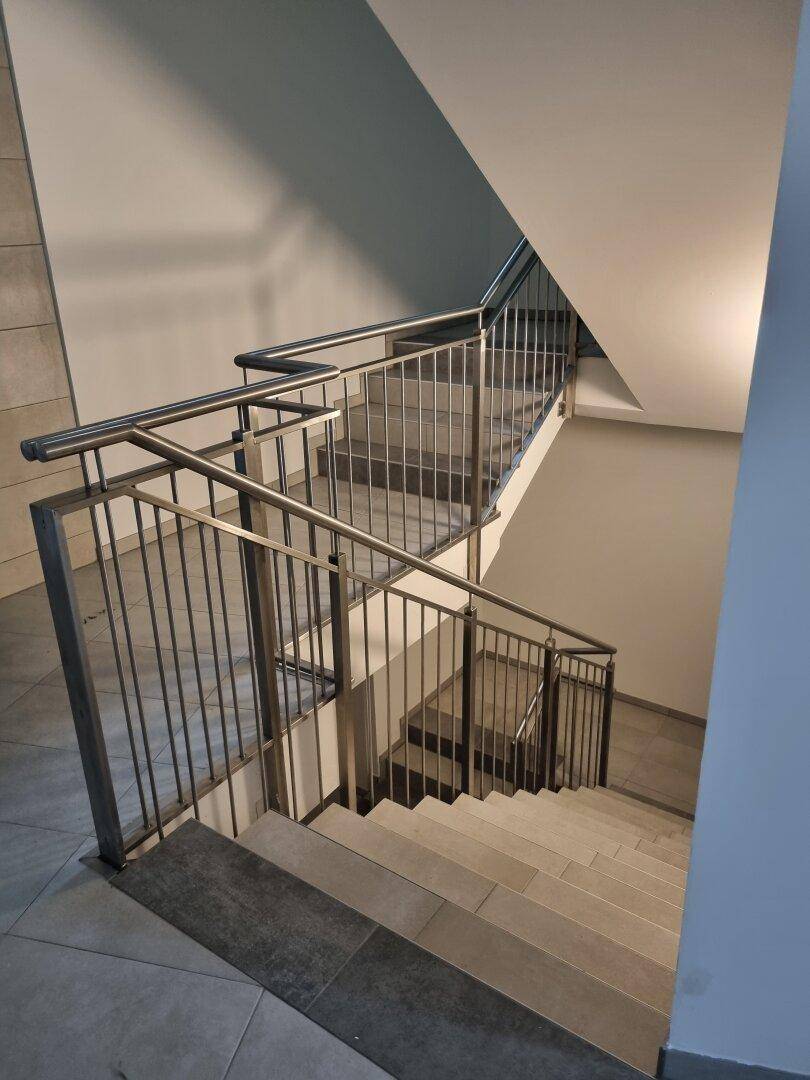 Modernes Treppenhaus mit Metallgeländer und Fliesenstufen in einem Mehrfamilienhaus.