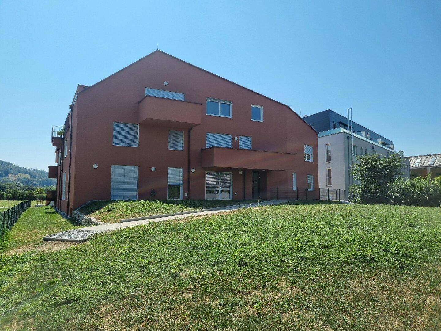 Gesamtansicht des modernen Wohngebäudes mit roter Fassade und umliegender Grünfläche.