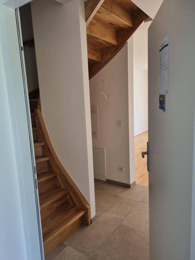 Eingangsbereich mit Holztreppe und Fliesenboden, der zu den oberen Etagen führt.