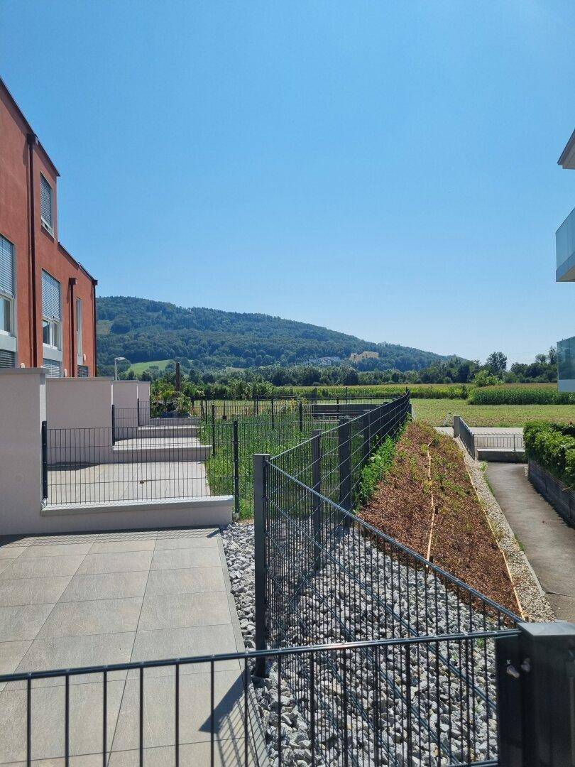 Terrasse mit Fliesenboden und weitem Blick auf die grüne Landschaft und angrenzende Gebäude.