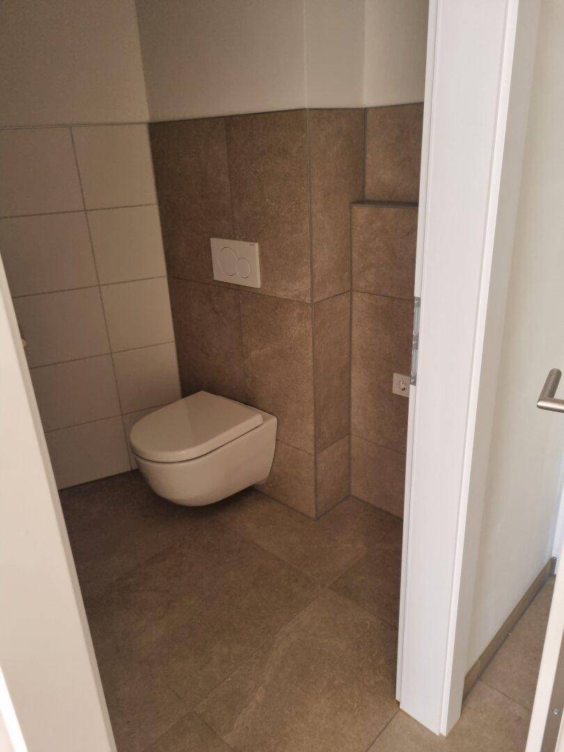 Modernes Gäste-WC mit Wand-WC und Fliesen an Wänden und Boden.