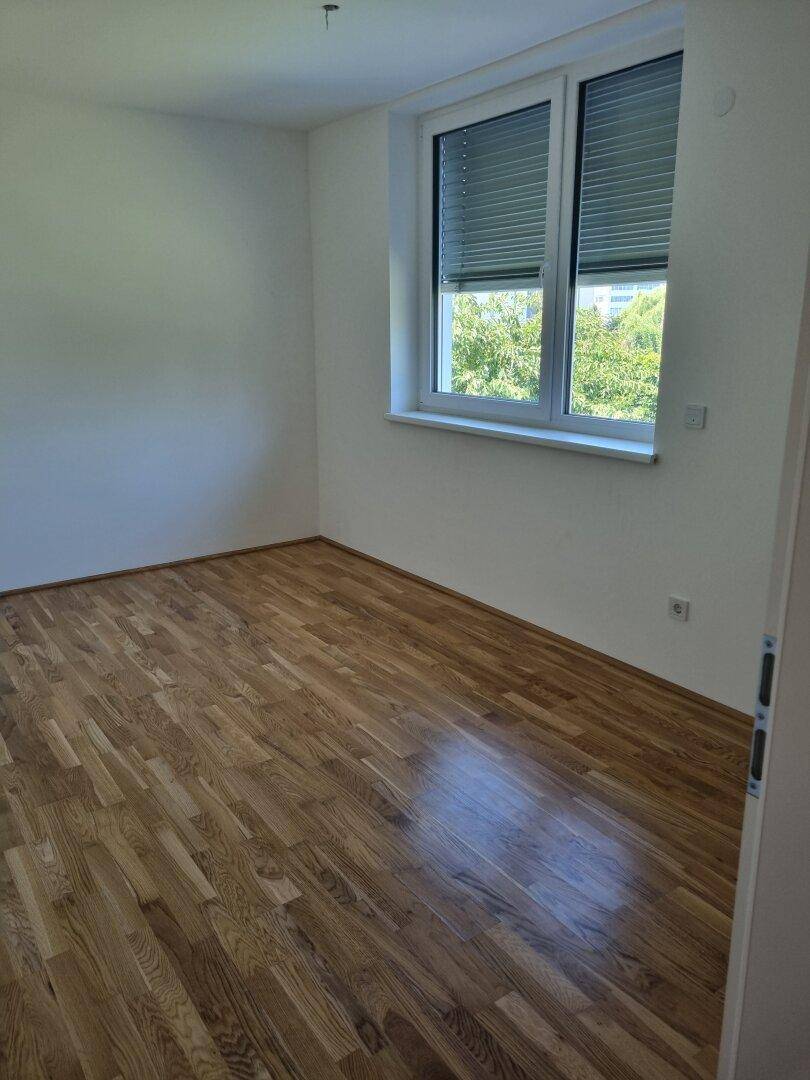 Helles Schlafzimmer mit Holzboden und Fenster, das viel Tageslicht hereinlässt.