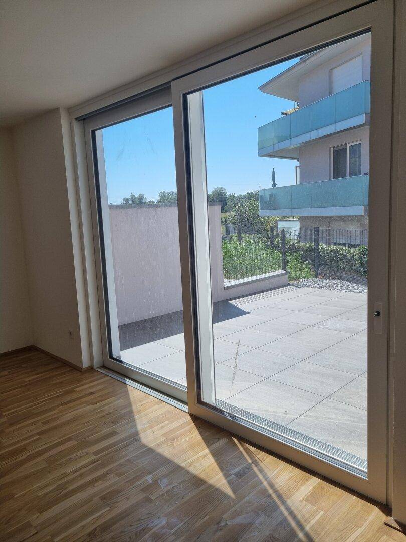Heller Raum mit Holzboden und großer Schiebetür zur Terrasse mit Blick auf Nachbargebäude.