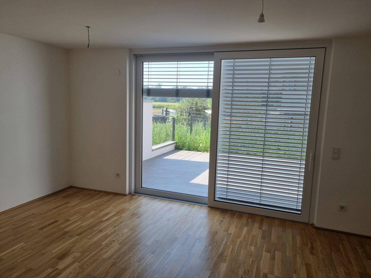 Heller Raum mit Holzboden und großer Schiebetür zur Terrasse mit Blick ins Grüne.