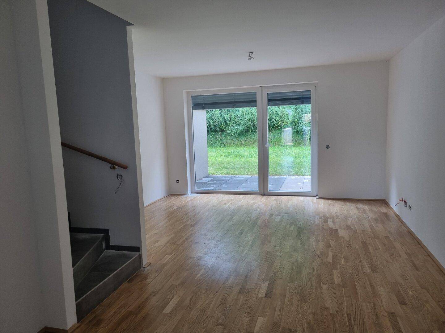 Heller, leerer Wohnraum mit Parkettboden und großem Fenster zum Garten.