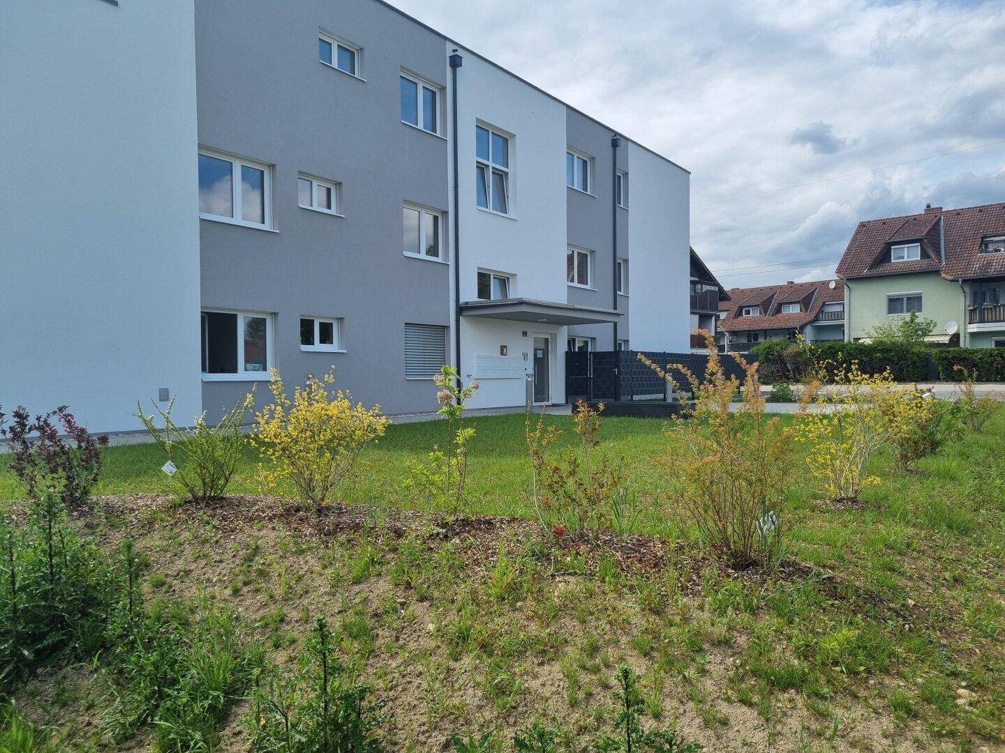 Modernes Wohngebäude mit weißer und grauer Fassade und junger Bepflanzung.