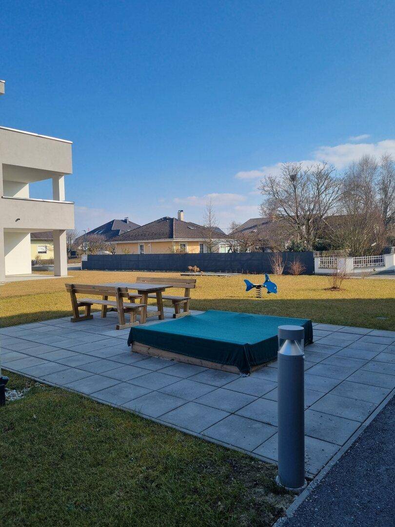 Gemeinschaftsgarten mit Sitzgelegenheiten und Sandkasten an einem sonnigen Tag.